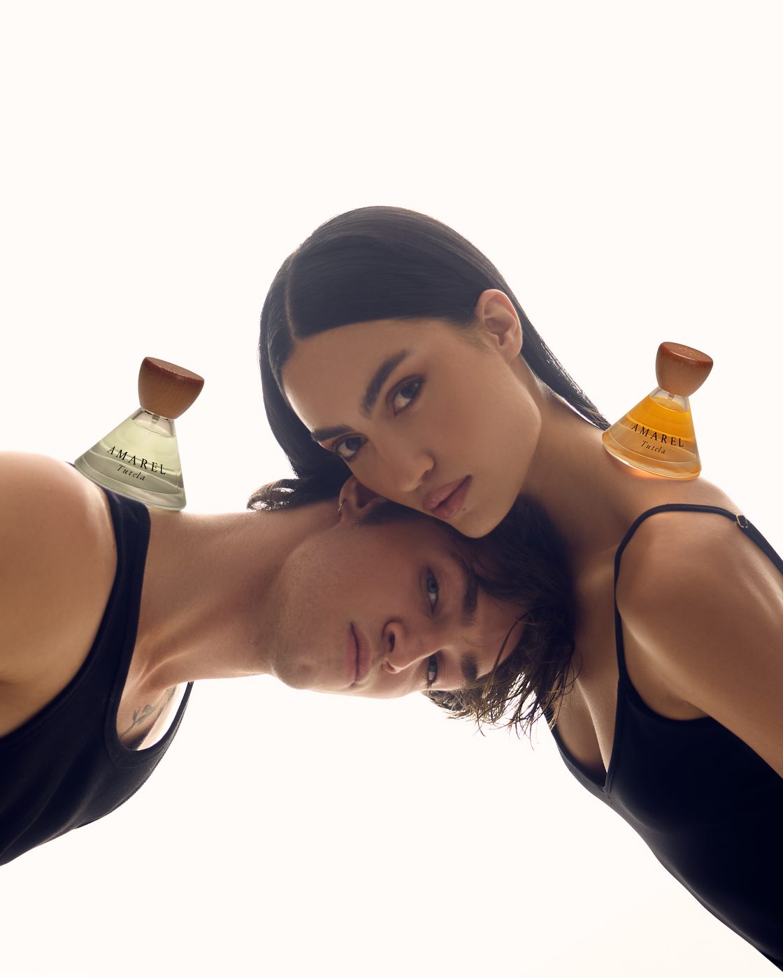 A man and a woman leaning head to head on white, Tutela 00 on his shoulder and Tutela 01 on hers