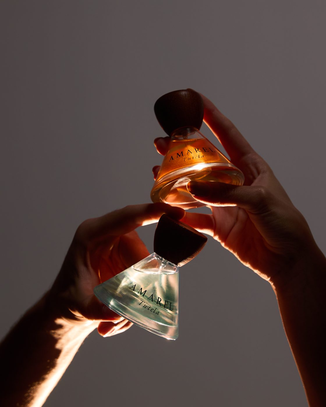 Two hands meeting with the two bottles of Tutela against grey