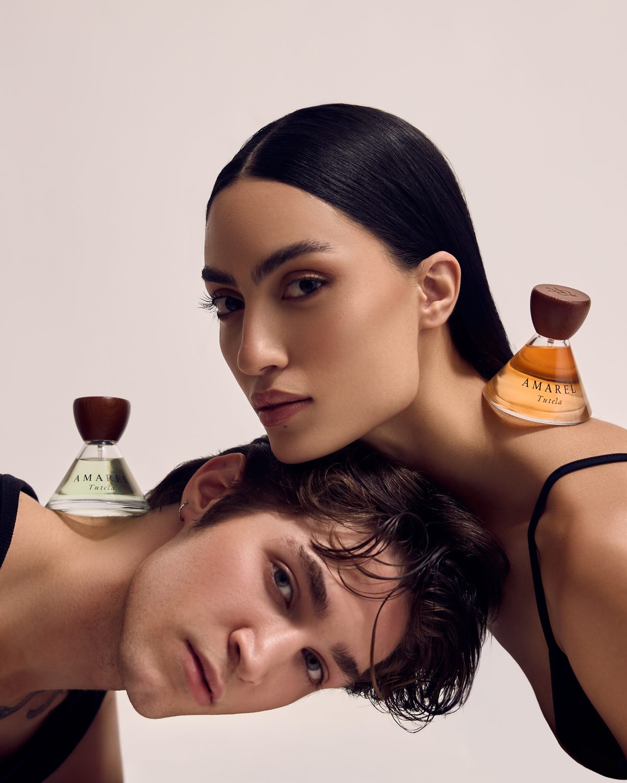 A man and a woman leaning head to head, a bottle of Tutela on each shoulder