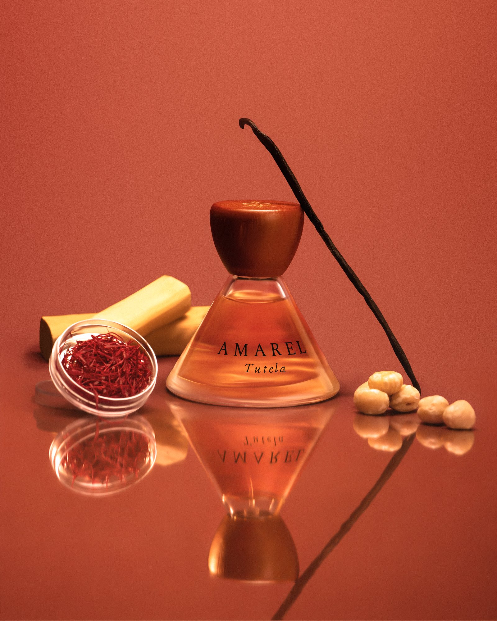 Tutela 01 standing on a mirror with saffron, sandalwood, a vanilla pod and hazelnuts, on terracotta